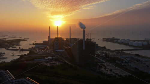 Copenhagen, Denmark – August 3, 2025: Aerial drone view of CopenHill chimneys with smoke rising against the orange sunrise sky in Copenhagen, Denmark - Starpik Stock
