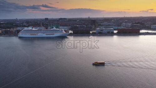 Copenhagen, Denmark – August 3, 2025: Aerial drone view of a cruise ship docked in Copenhagen harbor near Langelinie with a yellow harbor bus sailing nearby - Starpik Stock