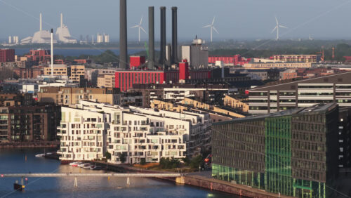 Copenhagen, Denmark – August 3, 2025: Aerial drone view of the Quay Bridge with modern waterfront apartments in Copenhagen, Denmark with canals and wind turbines in the distance - Starpik Stock