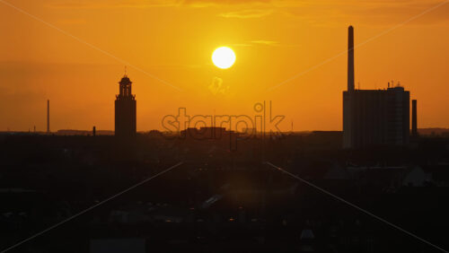Copenhagen, Denmark – August 3, 2025: Aerial drone view of the city’s skyline during sunset, with the sun glowing above landmarks and industrial chimneys silhouetted against the orange sky - Starpik Stock
