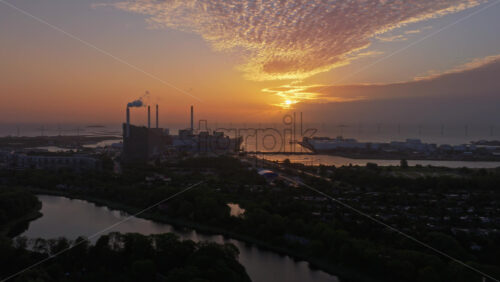 Copenhagen, Denmark – August 3, 2025: Aerial drone view of the sunrise with CopenHill chimneys, offshore wind turbines, and glowing skies - Starpik Stock