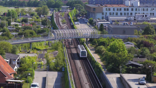 Copenhagen, Denmark – August 4, 2025: Aerial drone view of Oresund Metro Station from above, with a train arriving and cyclists on the overpass - Starpik Stock