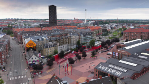 Copenhagen, Denmark – August 4, 2025: Aerial drone view of Superkilen Park with its signature red square and the Norrebrohallen cultural center - Starpik Stock