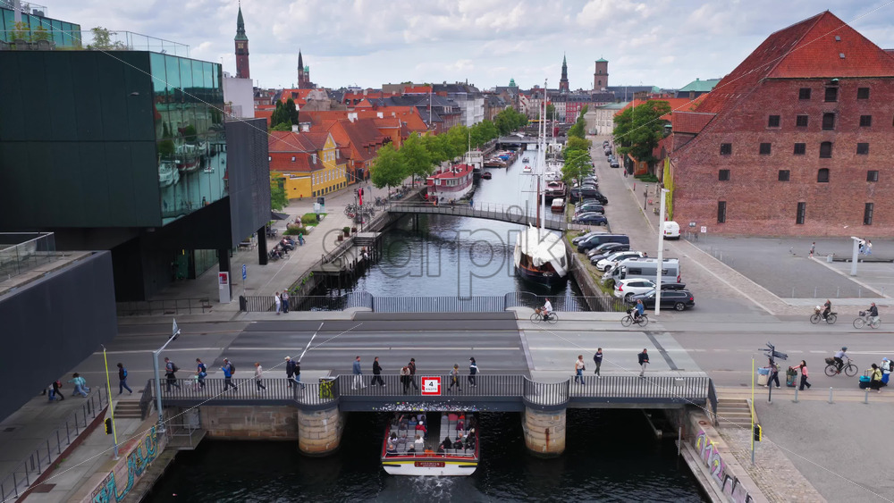Copenhagen, Denmark – August 4, 2025: Aerial drone view of a tourist boat passing under the bridge next to BLOX, with historic Copenhagen houses and canals in the background - Starpik Stock