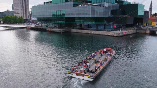 Copenhagen, Denmark – August 4, 2025: Aerial drone view of a tourist canal boat cruising under Lille Langebro bridge near the harborfront - Starpik Stock