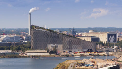 Copenhagen, Denmark – August 4, 2025: Aerial drone view of the Amager Bakke power plant with its artificial ski slope and smoke rising from the chimney - Starpik Stock