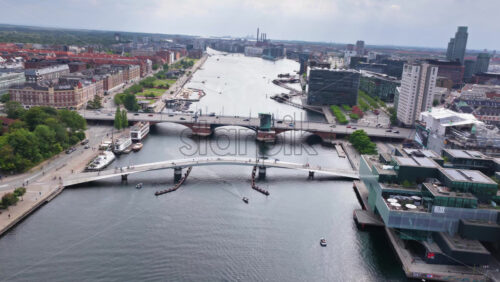 Copenhagen, Denmark – August 4, 2025: Aerial drone view of the curved pedestrian and cycling bridge spanning Copenhagen’s harbor, with Langebro bridge behind - Starpik Stock
