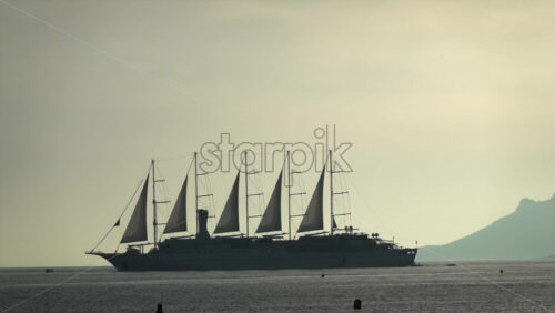 Distant view of a large multi-mast sailing ship gliding across the Mediterranean Sea at sunset with mountains on the background - Starpik Stock