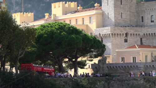 Distant view of the Prince’s Palace of Monaco and medieval ramparts perched above Monaco, with visitors walking around - Starpik Stock