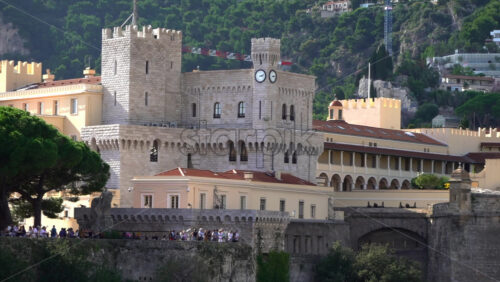 Distant view of the Prince’s Palace of Monaco and medieval ramparts perched above Monaco, with visitors walking around - Starpik Stock