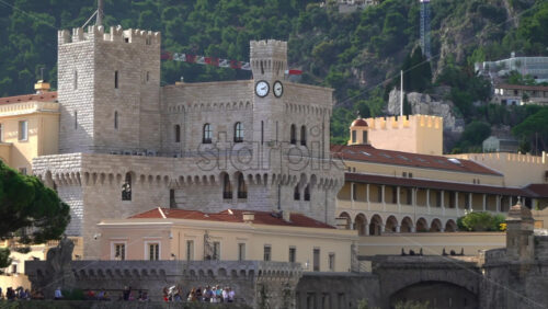 Distant view of the Prince’s Palace of Monaco and medieval ramparts perched above Monaco, with visitors walking around - Starpik Stock