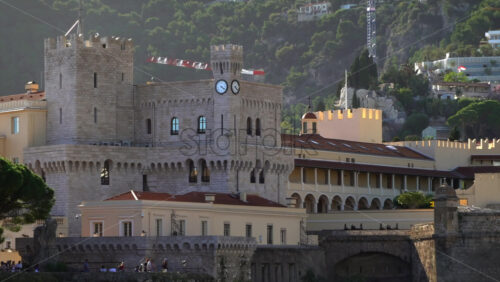 Distant view of the Prince’s Palace of Monaco and medieval ramparts perched above Monaco, with visitors walking around - Starpik Stock