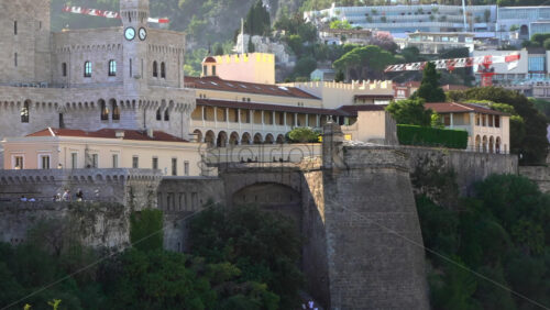 Distant view of the Prince’s Palace of Monaco and medieval ramparts perched above Monaco, with visitors walking around - Starpik Stock