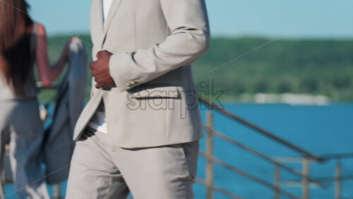 Elegantly dressed man and woman walking on a scenic terrace with a view of a calm body of water - Starpik Stock