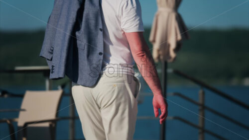 Elegantly dressed man walking on a scenic terrace with a view of a calm body of water - Starpik Stock