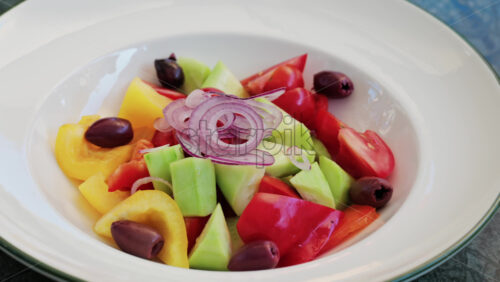 Fresh Greek salad served in a white plate with cucumbers, tomatoes, bell peppers, red onion rings, and Kalamata olives - Starpik Stock