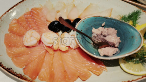 Fresh seafood platter with smoked salmon slices, shrimp, olives, and pate served with lemon and dill garnish - Starpik Stock
