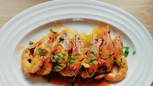 Garlic prawns in a rich sauce topped with herbs on a white plate - Starpik Stock