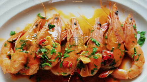 Garlic prawns in a rich sauce topped with herbs on a white plate - Starpik Stock