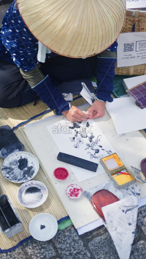 Gion, Japan – April 11, 2025: Old person wearing a traditional Japanese hat painting in black and white on the street. Vertical - Starpik Stock