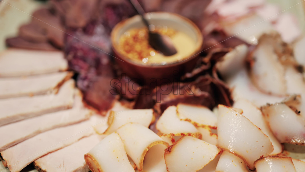 Gourmet charcuterie board with assorted cured meats, smoked slices, and a mustard seed sauce served in a bowl - Starpik Stock