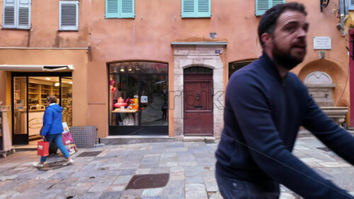 Grasse, France – August 10, 2025: Picturesque street decorated with pink umbrellas hanging above, surrounded by charming boutiques and people strolling - Starpik Stock
