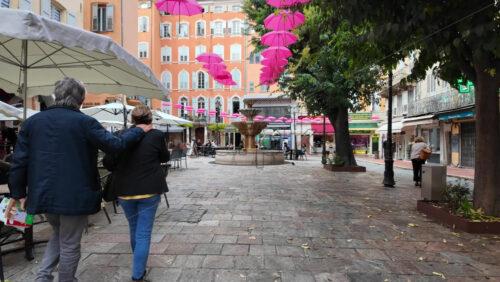 Grasse, France – August 10, 2025: Picturesque street decorated with pink umbrellas hanging above, surrounded by charming boutiques and people strolling - Starpik Stock