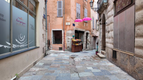 Grasse, France – August 10, 2025: Picturesque street decorated with pink umbrellas hanging above, surrounded by charming boutiques and people strolling - Starpik Stock
