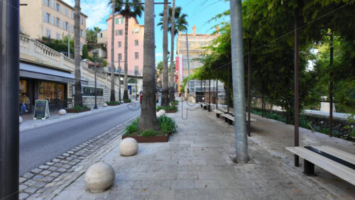 Grasse, France – August 10, 2025: Scenic city street in the city lined with palm trees, shops, and cafes, with cars and people passing by - Starpik Stock