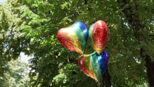 Heart-shaped balloons with a rainbow pattern with green trees on the background - Starpik Stock