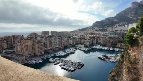 High-angle view of Port de Fontvieille in Monaco, showcasing colorful buildings, luxury yachts, and the surrounding mountainous landscape - Starpik Stock
