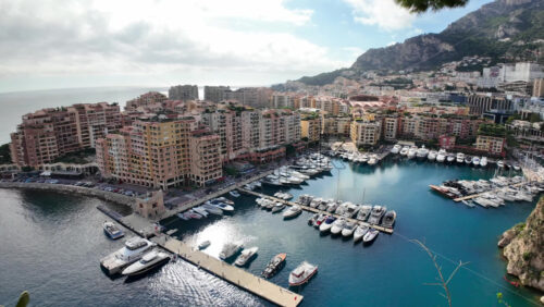 High-angle view of Port de Fontvieille in Monaco, showcasing colorful buildings, luxury yachts, and the surrounding mountainous landscape - Starpik Stock
