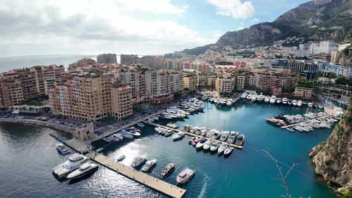 High-angle view of Port de Fontvieille in Monaco, showcasing colorful buildings, luxury yachts, and the surrounding mountainous landscape - Starpik Stock