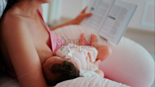 Intimate close up of a mother breastfeeding her baby while holding a book - Starpik Stock