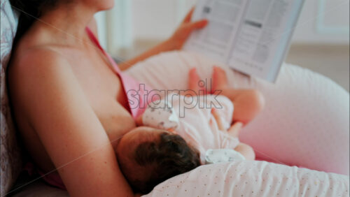 Intimate close up of a mother breastfeeding her baby while holding a book - Starpik Stock