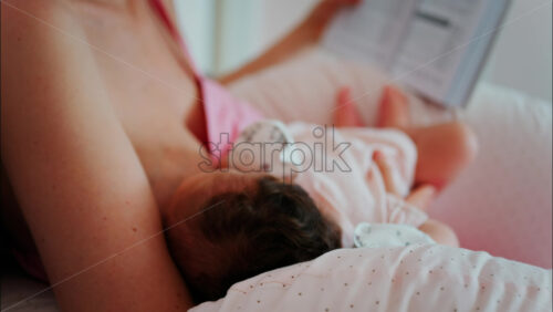 Intimate close up of a mother breastfeeding her baby while holding a book - Starpik Stock