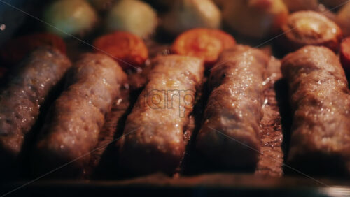 Juicy meat rolls grilling in the oven alongside carrots and potatoes, sizzling in high heat - Starpik Stock
