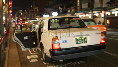 Kyoto, Japan – April 11, 2025: White taxi waiting on the street with the door open in the Gion area in the evening. Translation: “Taxi attendant recruitment” - Starpik Stock