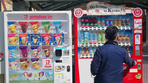 Kyoto, Japan – April 12, 2025: Man buying a drink from a vending machine on the street in the Gion area in daylight. Translation: “Book free, download soon, you can buy it with QR” - Starpik Stock