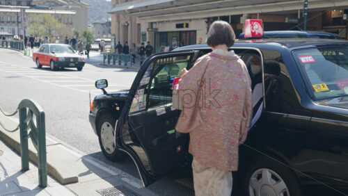 Kyoto, Japan – April 12, 2025: Woman getting in a taxi on the street and leaving in the Gion area in daylight. Translation: “Shijo Ohashi bridge” - Starpik Stock