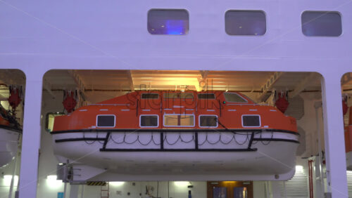 La Condamine, Monaco – July 4, 2025: Close-up of bright orange lifeboats secured on the side of a cruise ship, illuminated by soft evening lighting - Starpik Stock