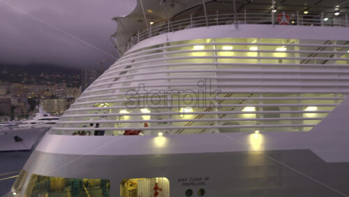 La Condamine, Monaco – July 4, 2025: Evening view of a cruise ship docked in Monaco, with illuminated decks and the city skyline in the background under a cloudy sky - Starpik Stock