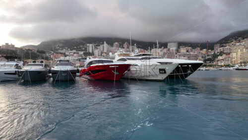 La Condamine, Monaco – July 4, 2025: Row of sleek luxury yachts, docked in Port Hercules with the Monaco cityscape and misty hills in the background - Starpik Stock