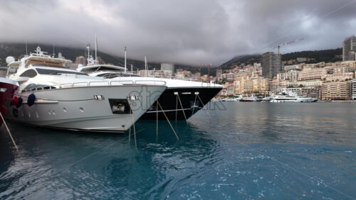 La Condamine, Monaco – July 4, 2025: Row of sleek luxury yachts, docked in Port Hercules with the Monaco cityscape and misty hills in the background - Starpik Stock