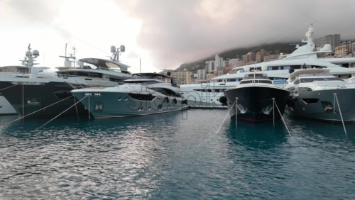 La Condamine, Monaco – July 4, 2025: Row of sleek luxury yachts, docked in Port Hercules with the Monaco cityscape and misty hills in the background - Starpik Stock