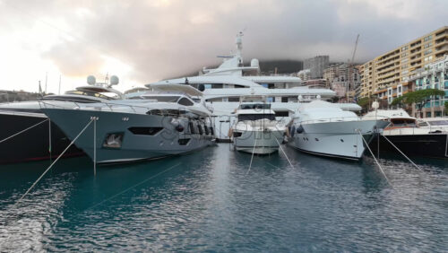 La Condamine, Monaco – July 4, 2025: Row of sleek luxury yachts, docked in Port Hercules with the Monaco cityscape and misty hills in the background - Starpik Stock