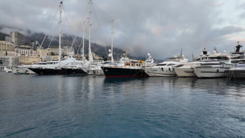 La Condamine, Monaco – July 4, 2025: Row of sleek luxury yachts, docked in Port Hercules with the Monaco cityscape and misty hills in the background - Starpik Stock