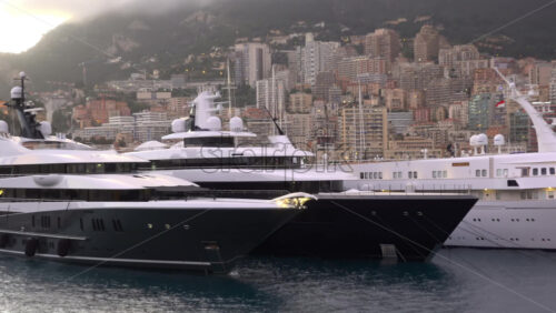 La Condamine, Monaco – July 4, 2025: Row of sleek luxury yachts, docked in Port Hercules with the Monaco cityscape and misty hills in the background - Starpik Stock
