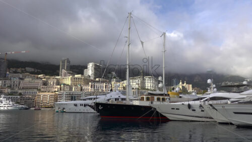 La Condamine, Monaco – July 4, 2025: Row of sleek luxury yachts, docked in Port Hercules with the Monaco cityscape and misty hills in the background - Starpik Stock