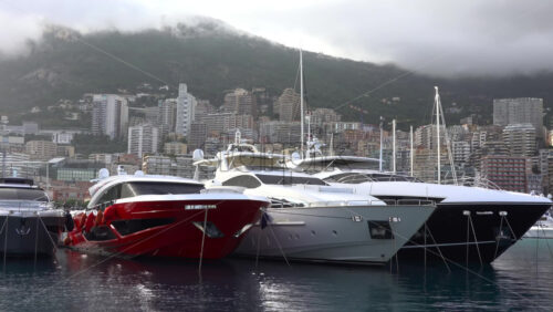 La Condamine, Monaco – July 4, 2025: Row of sleek luxury yachts, docked in Port Hercules with the Monaco cityscape and misty hills in the background - Starpik Stock